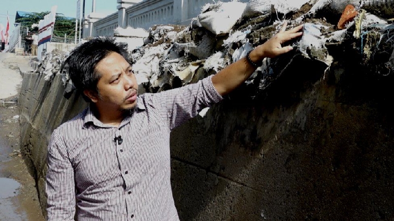 Heri Andreas points at a dyke built to prevent sea water from flooding houses when it rains